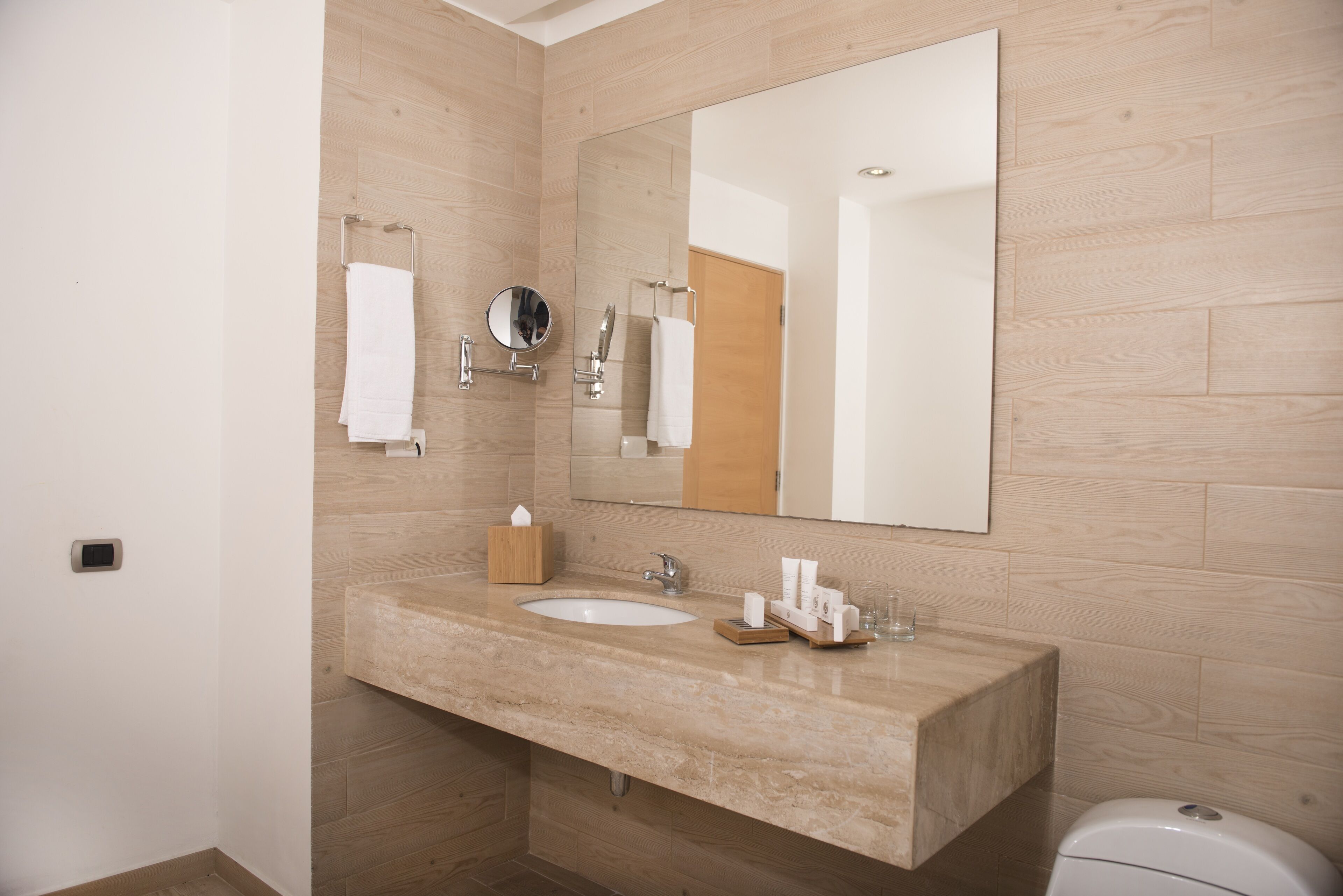 Un baño moderno con lavamanos de mármol, un espejo grande y un mueble de tocador de madera.
