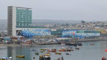 A coastal cityscape with a prominent modern building featuring a blue and white patterned facade, a marina with numerous boats, and a densely populated urban background.