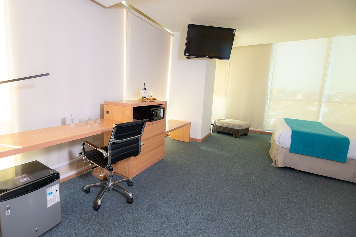 Une chambre d’hôtel équipée d’un bureau, d’une chaise, d’une télévision, d’un lit et d’une fenêtre donnant sur un paysage agréable.