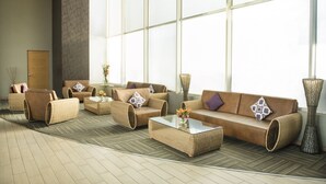 Um hall amplo com uma grande janela, um conjunto de sofás, uma mesa de centro e um vaso decorativo.