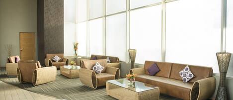 Um hall amplo com uma grande janela, um conjunto de sofás, uma mesa de centro e um vaso decorativo.