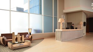 Um hall de hotel moderno com uma mesa de recepção, um sofá de couro marrom e uma mesa de centro de vidro com vasos decorativos.