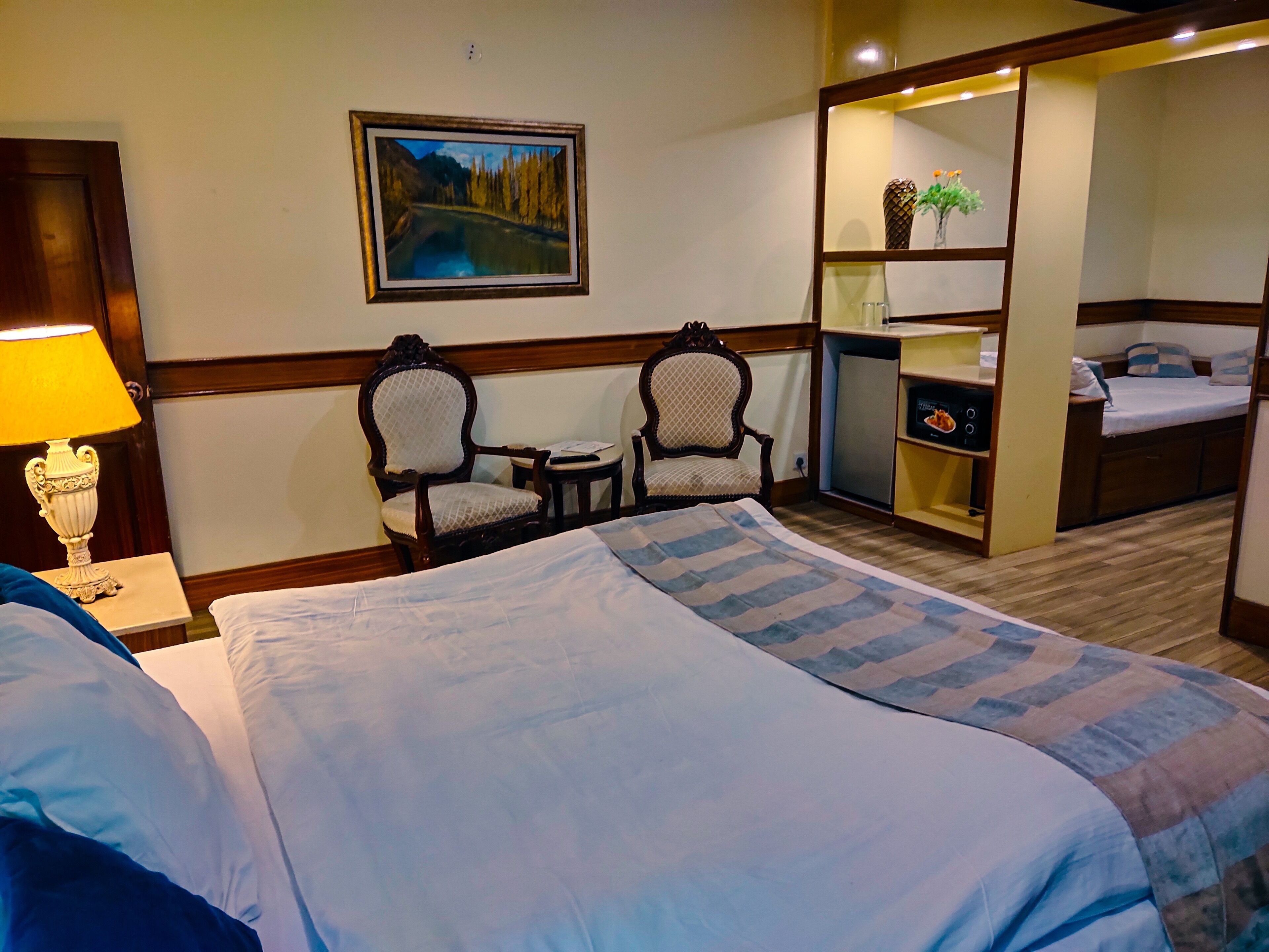 Habitación de hotel con una cama grande, dos sillones, una mesita, un cuadro en la pared y una zona de kitchenette.