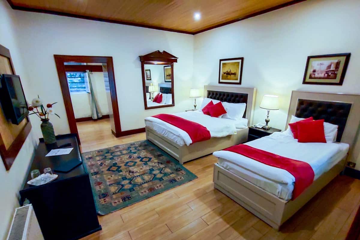 Une chambre d’hôtel avec deux lits, un plancher en bois, un tapis, un bureau avec un vase et un miroir.