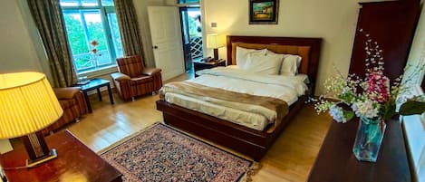Una habitación de hotel con una cama grande, un escritorio con lámpara, una silla, un tapete y una ventana con cortinas.