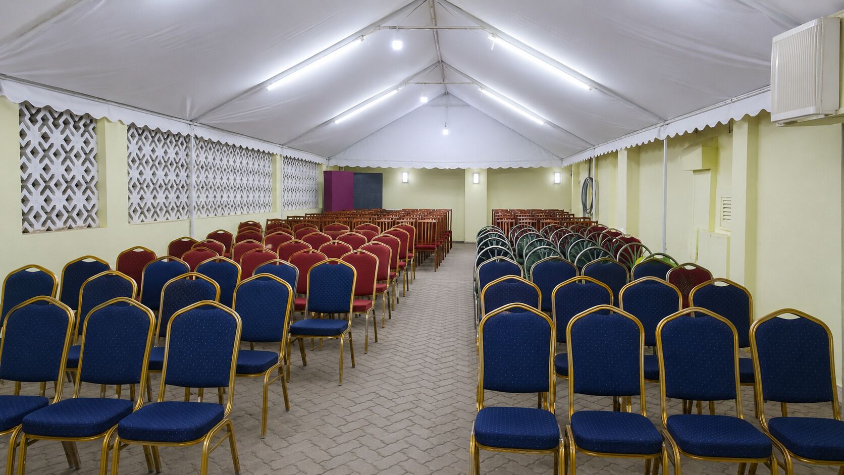 A large hall with rows of blue and red chairs, white ceiling, and patterned wall decorations.