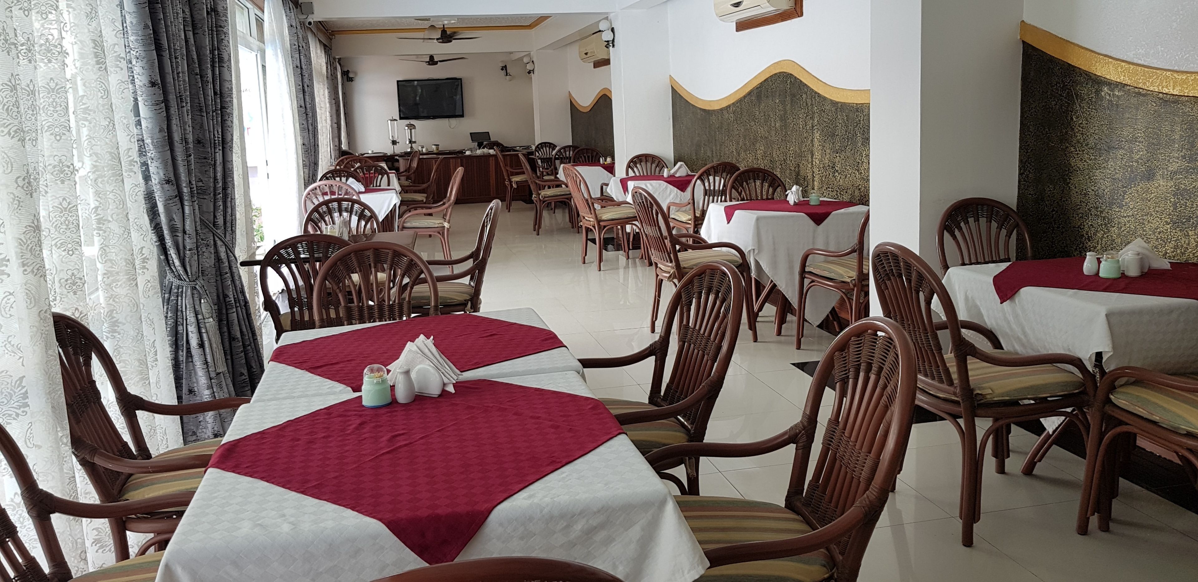 A restaurant with multiple tables and chairs, a bar area, and a television screen on the wall.
