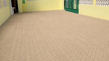 Um pátio com piso pavimentado, portão verde e um edifício azul com placa de estacionamento.