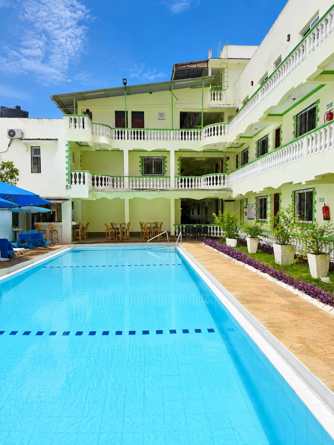 Un hotel con piscina, mobiliario exterior y un edificio de varios pisos con balcones.