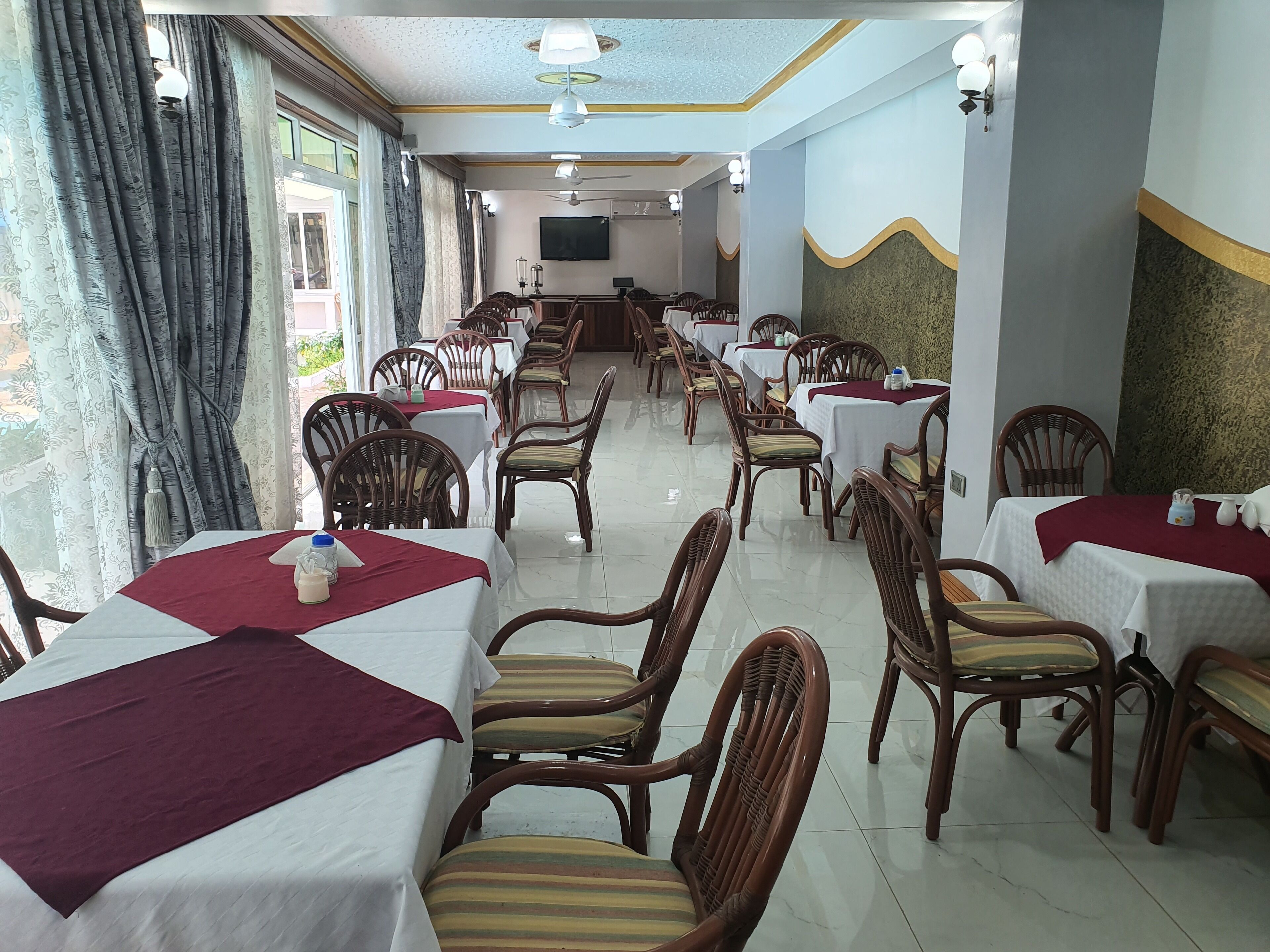 A restaurant with multiple tables and chairs, a ceiling fan, and a television on the wall.