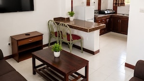 Un salon avec un téléviseur, une table à manger avec des chaises, un coin cuisine avec des placards et un ventilateur de plafond.