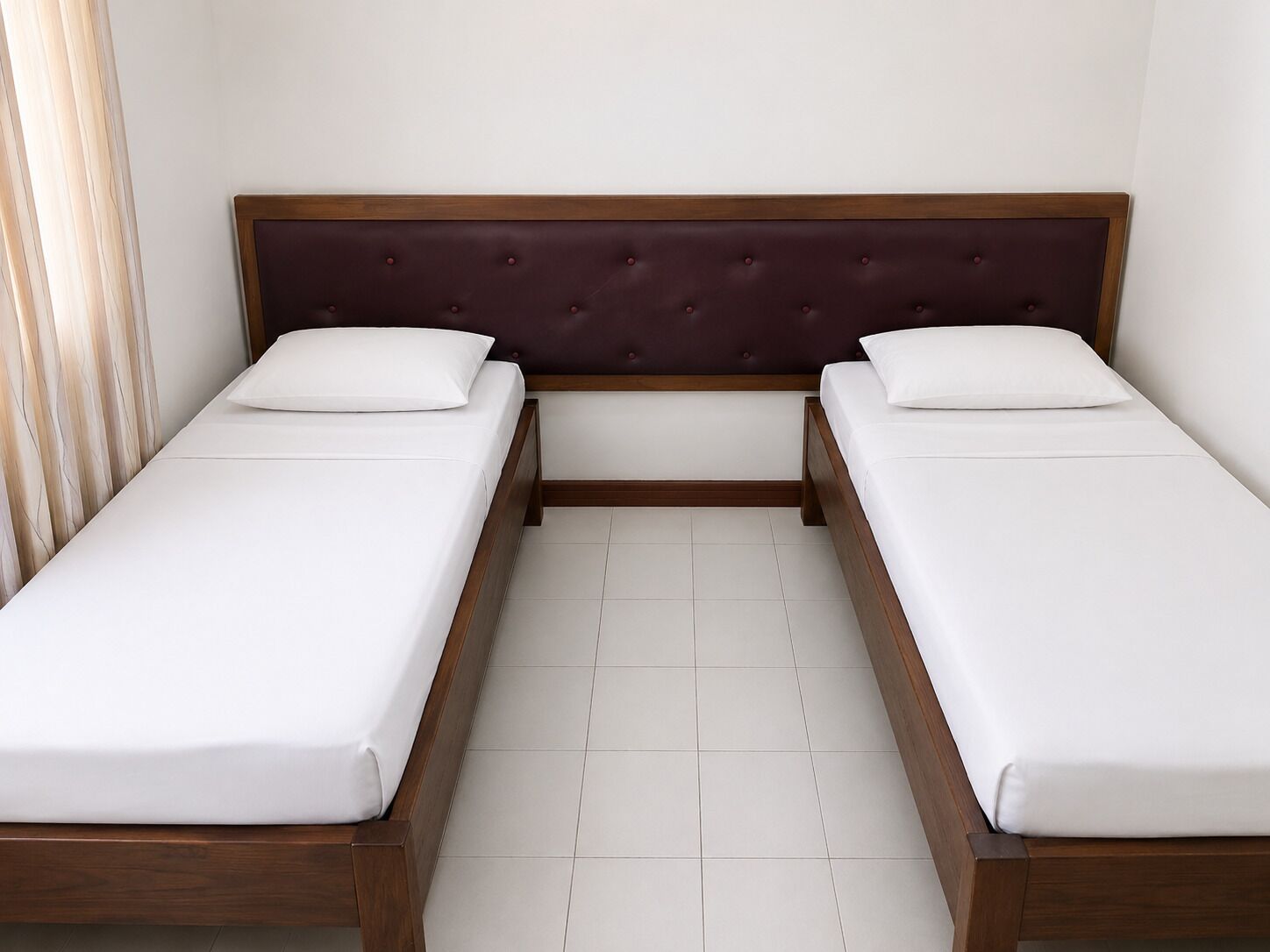 A double bed with a wooden frame and a dark headboard, two white pillows, and a tiled floor.
