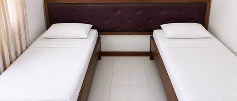 A double bed with a wooden frame and a dark headboard, two white pillows, and a tiled floor.