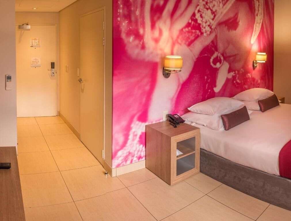 Ein Hotelzimmer mit Bett, Nachttischlampen, einem Nachttisch und einer Wand mit einem abstrakten rosafarbenen Design.