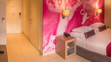 Ein Hotelzimmer mit Bett, Nachttischlampen, einem Nachttisch und einer Wand mit einem abstrakten rosafarbenen Design.