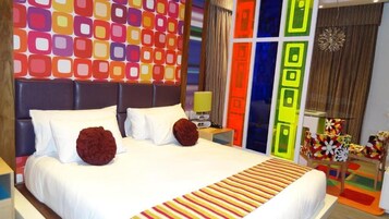 A hotel room with a large bed, a headboard with a geometric pattern, a bedside table with a lamp, and a colorful wall decoration.