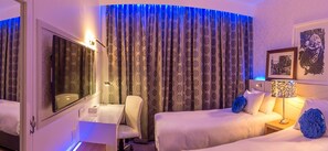 Habitación de hotel con dos camas, un escritorio, una silla y un amplio ventanal con cortinas.