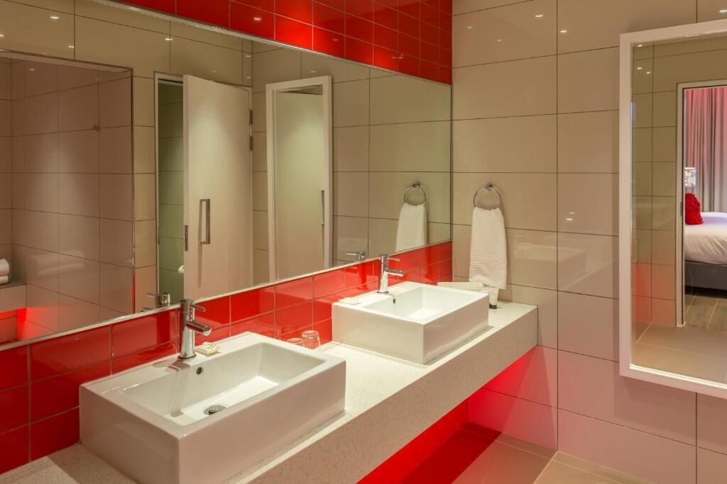 Un baño moderno con dos lavamanos, un espejo grande y detalles de iluminación roja.