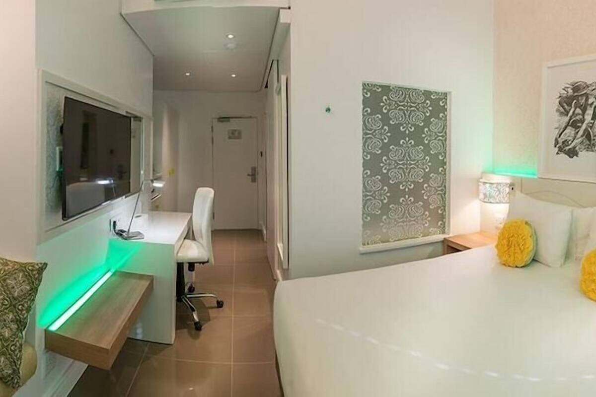 Una habitación de hotel con cama, escritorio, silla y obras de arte en las paredes.