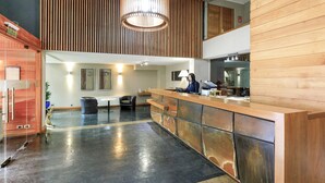 A modern reception area with a wooden reception desk, a receptionist, and a seating area with two chairs. - Hotel Frontera Plaza (Temuco)