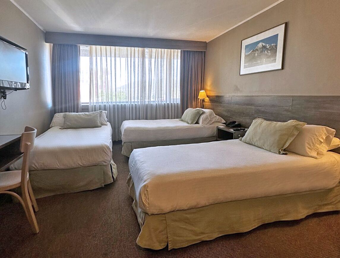 Een hotelkamer met twee eenpersoonsbedden, een bureau, een stoel, een televisie en een raam met gordijnen.
