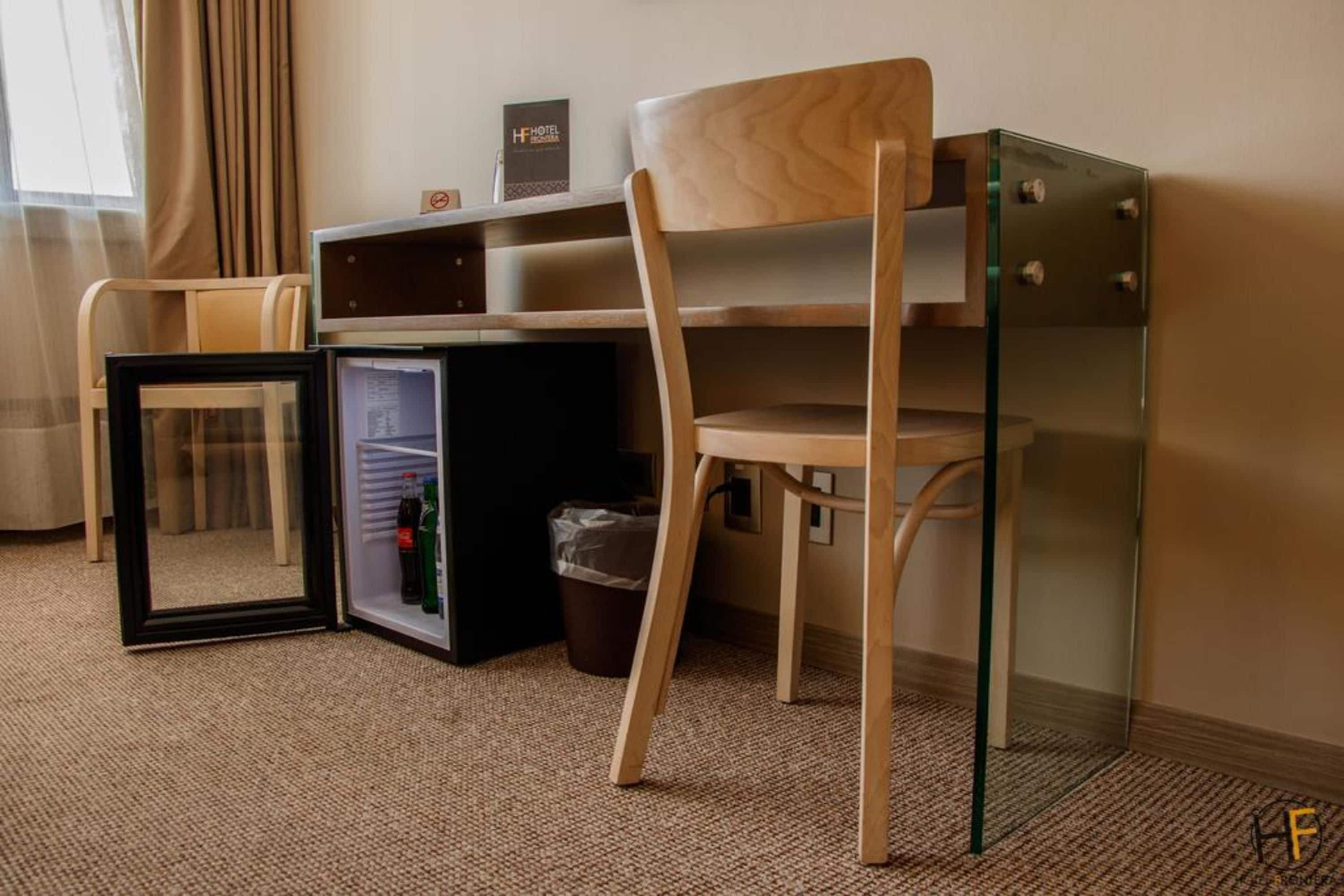 Habitación de hotel compacta con escritorio de vidrio, una silla, un refrigerador pequeño y un cesto de basura.
