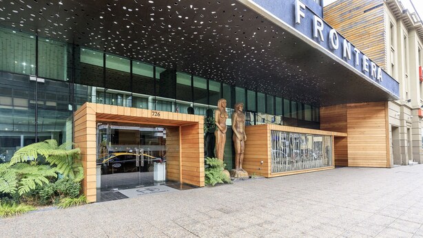A modern building entrance with a glass facade, wooden accents, and a sign reading "FRONTERA". - Hotel Frontera Plaza (Temuco)
