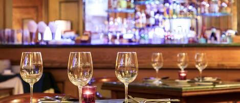 A bar area with multiple tables set for dining, each with wine glasses, cutlery, and candles.