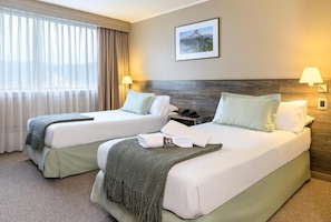 A hotel room with two beds, a large window with curtains, a framed picture on the wall, and two bedside lamps. - Hotel Frontera Plaza (Temuco)