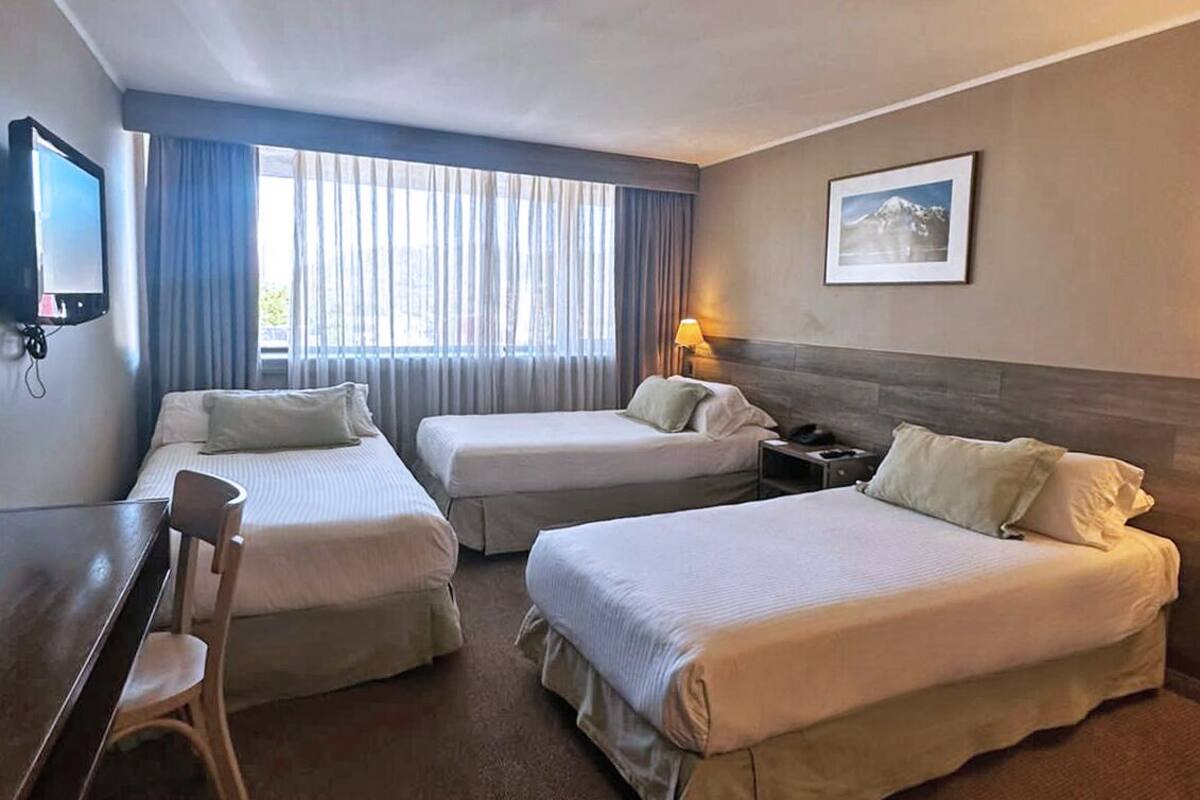 A hotel room with two single beds, a desk, a chair, a TV, and a window with curtains.