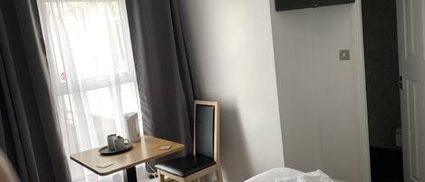 A hotel room with a bed, a desk with a chair, a television mounted on the wall, and a window with curtains.