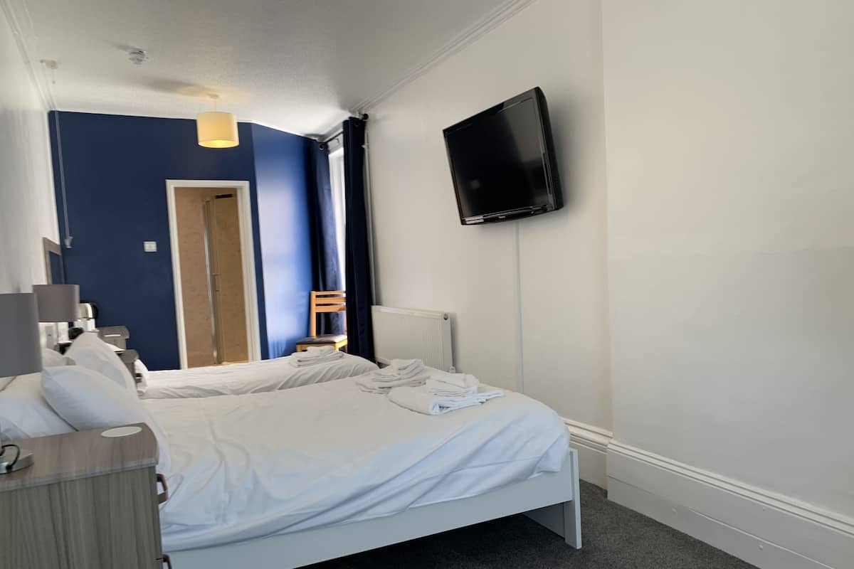 A hotel room with a bed, a TV mounted on the wall, a wooden chair, and a desk with a lamp.