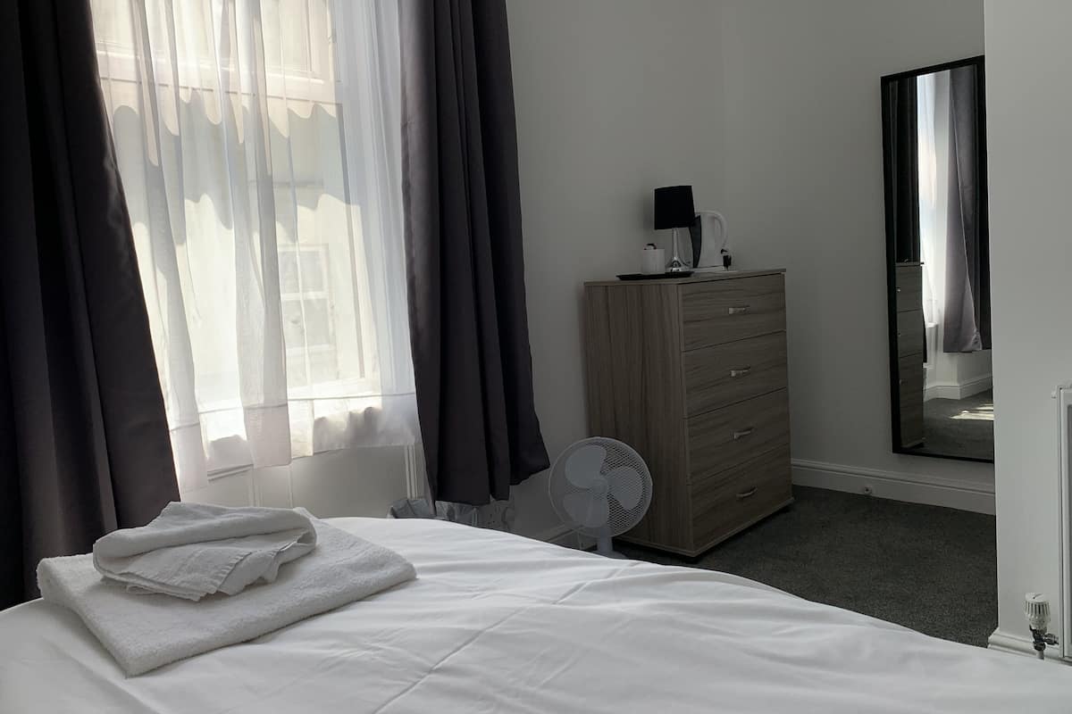 A hotel room with a bed, a dresser, a fan, and a mirror.