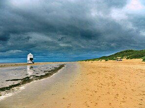 Una playa con un faro, orilla arenosa y cielo nublado.