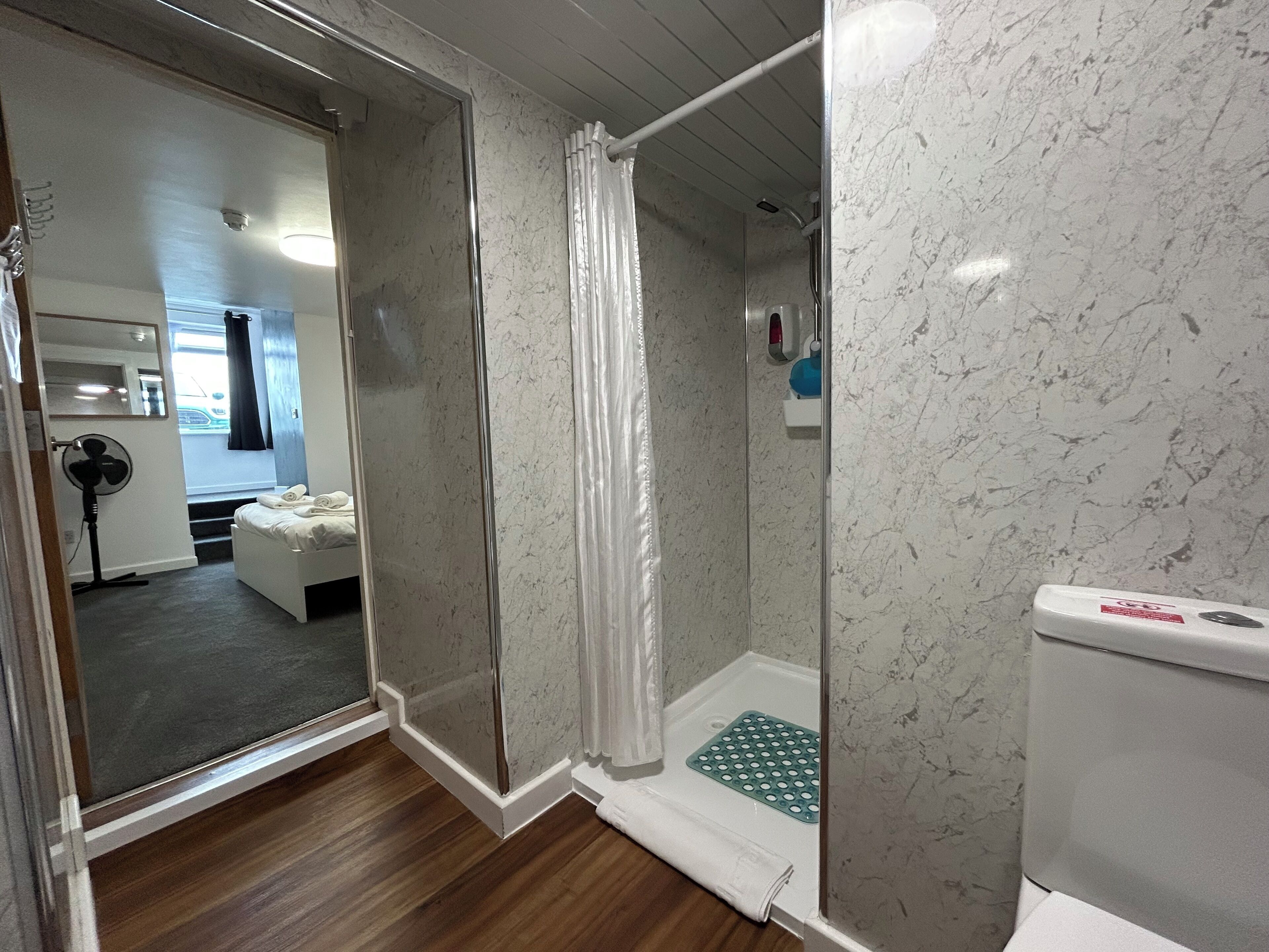 A modern bathroom with a glass-enclosed shower, a white toilet, and a wooden floor.