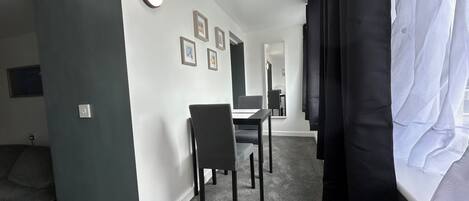 A modern hotel room with a grey carpet, a dining area with a table and chairs, and a large mirror on the wall.