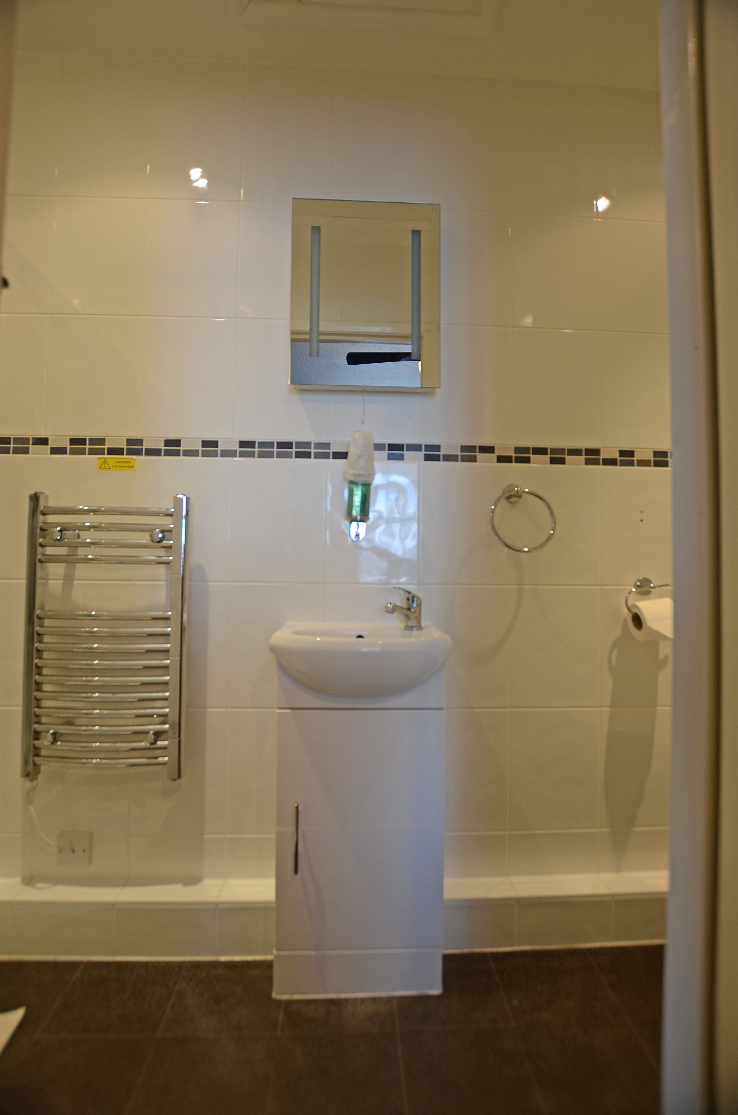 A bathroom with a sink, mirror, towel rack, and toilet paper holder.