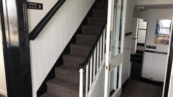 Una escalera con barandales negros y peldaños alfombrados que conduce a un cuarto con una puerta blanca y un letrero que indica las habitaciones 11 a 13.