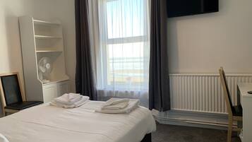 Habitación de hotel con cama, escritorio con computadora, televisor en la pared y ventana con cortinas.