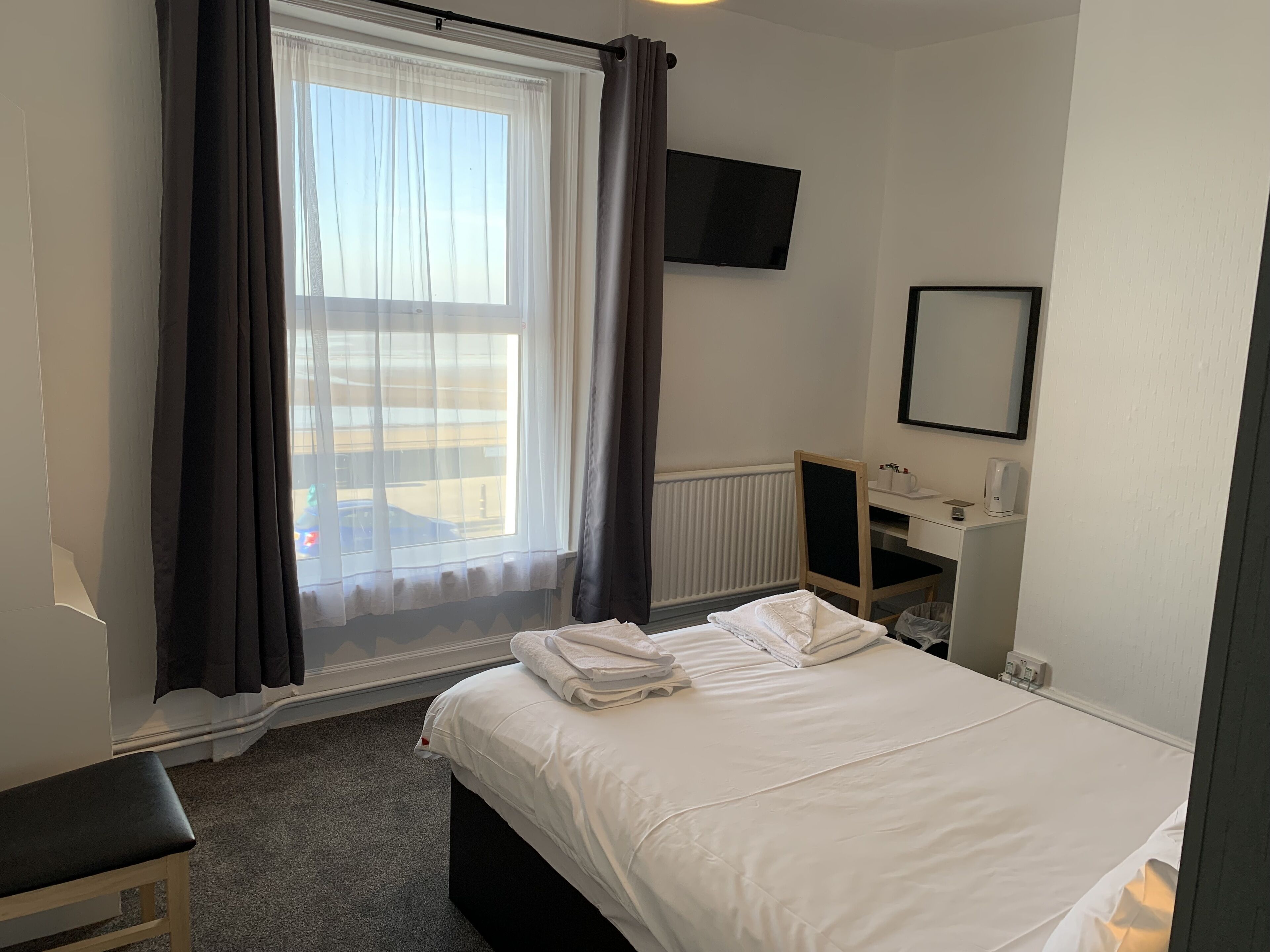 Ett hotellrum med en säng, ett skrivbord, en stol, en tv och ett fönster med gardiner.