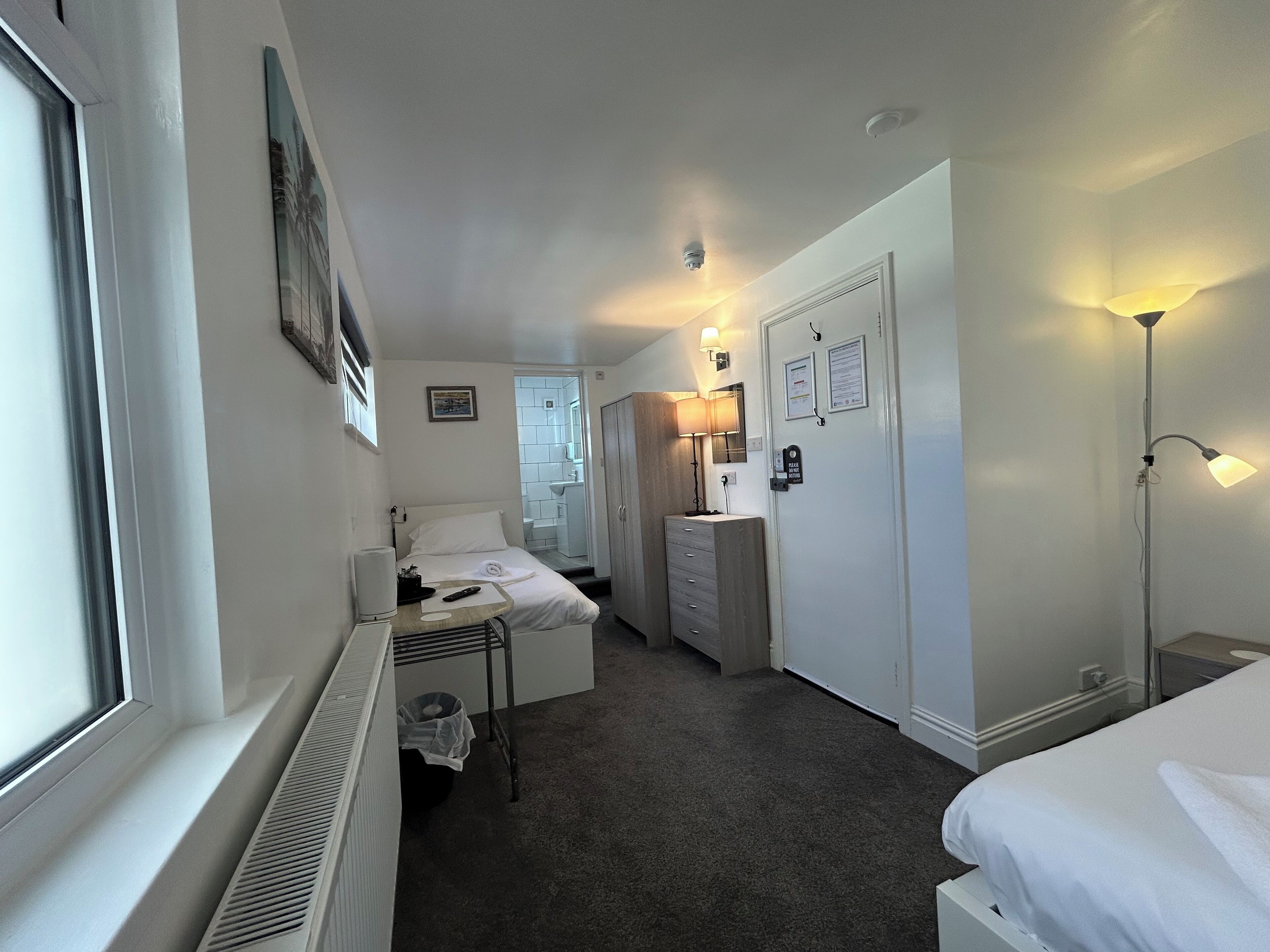 A hotel room with a bed, bedside table, lamp, and a view of the bathroom.