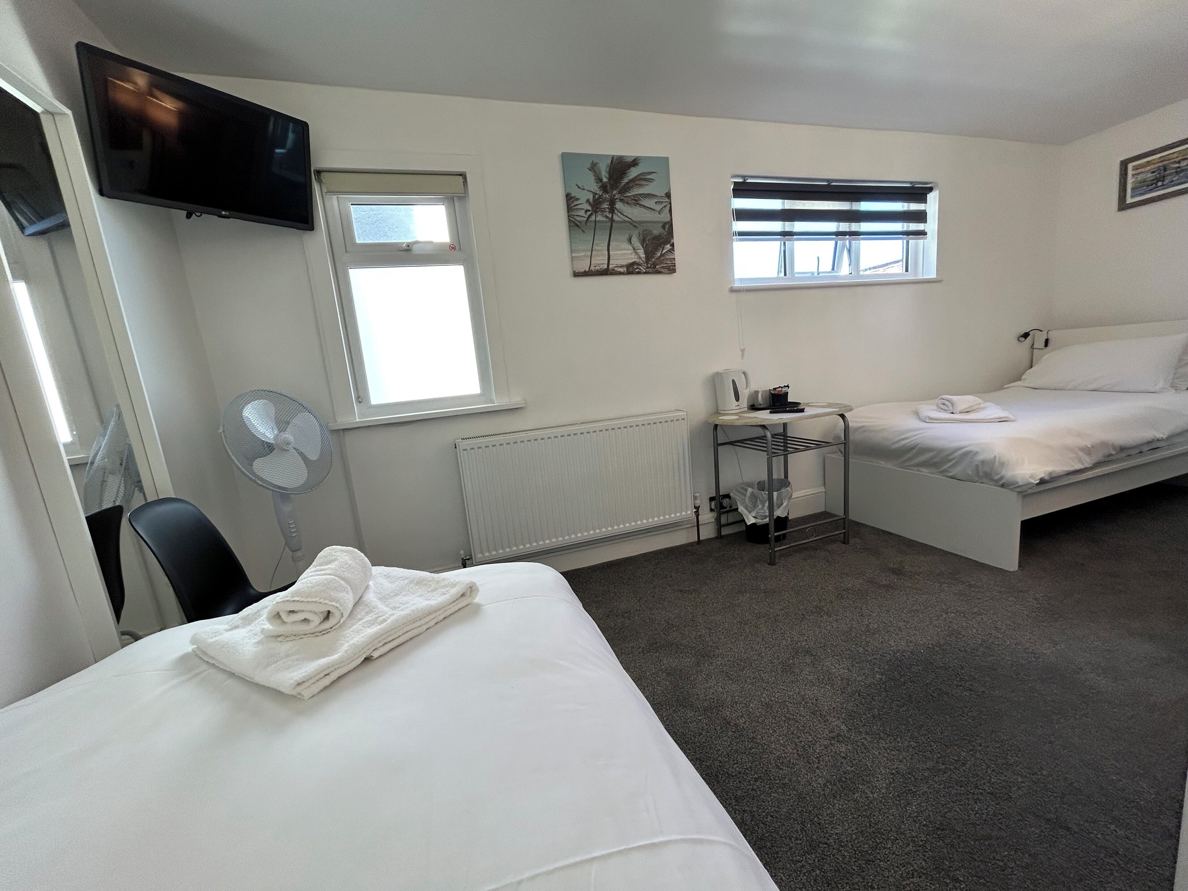 Une chambre d’hôtel avec un lit, un bureau, une chaise, une télévision et deux fenêtres.