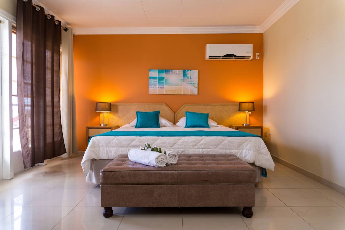 Een hotelkamer met een groot bed, twee nachtkastjes, een wandairconditioner en een raam met gordijnen.