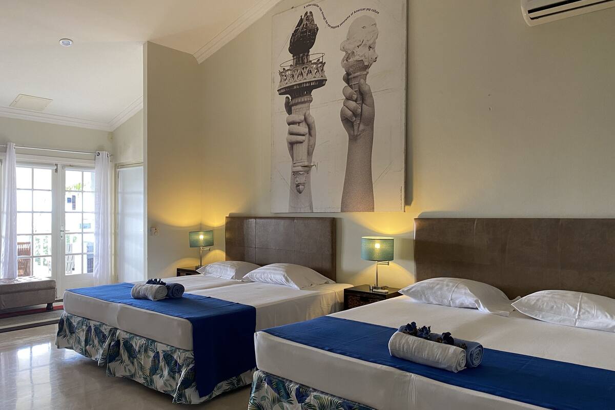 Een hotelkamer met twee bedden, elk met een blauwe sprei en passende hoofdeinden. Er zijn twee nachtkastjes met lampen, en een groot kunstwerk in een lijst boven de bedden.