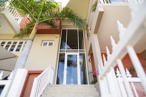 A building entrance with a glass door, a palm tree, and a white railing. - O Casarao Guesthouse (Willemstad)
