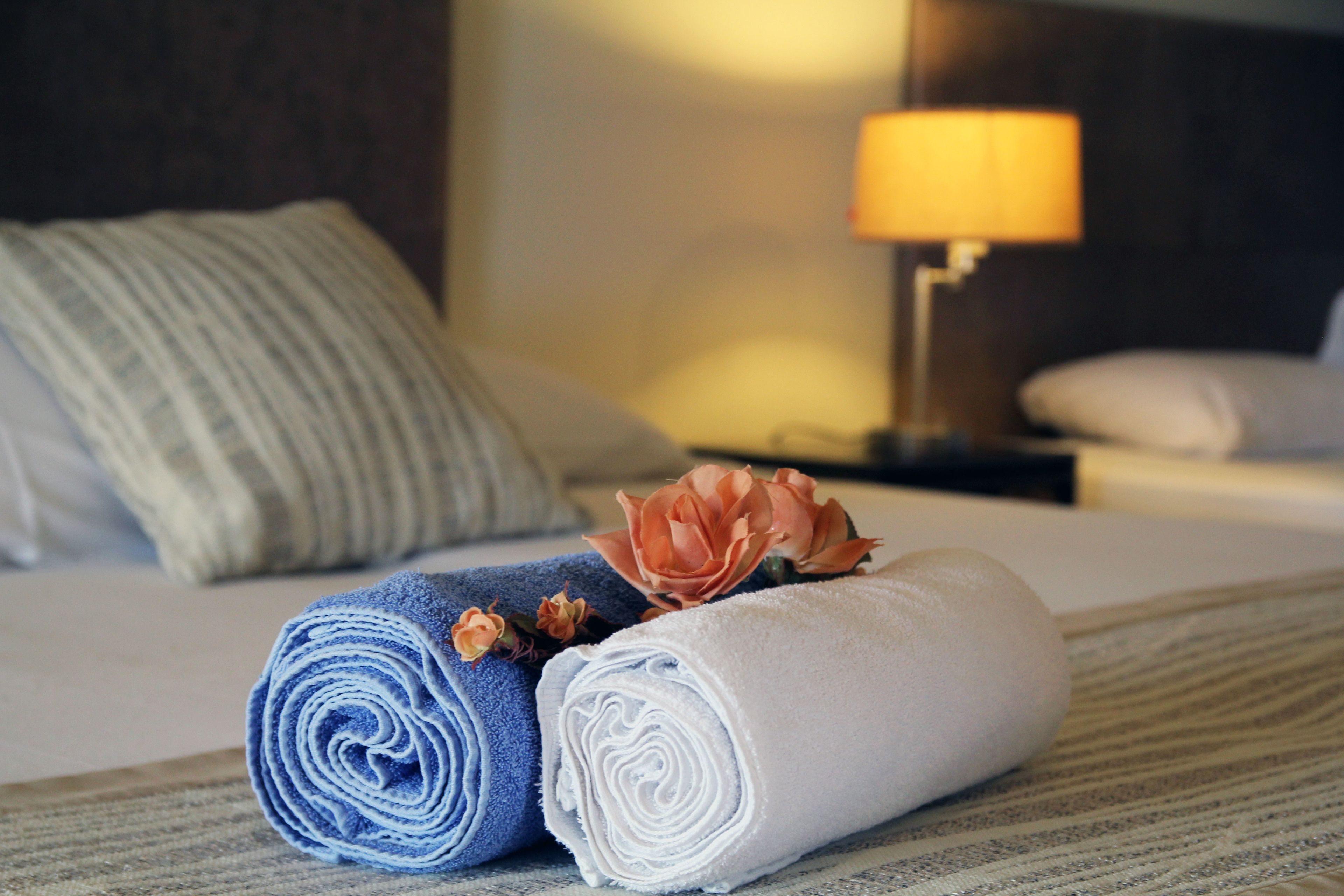 Una cama bien hecha con toallas enrolladas, una flor, una lámpara y una almohada en una habitación de hotel.