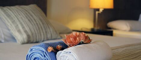 Una cama bien hecha con toallas enrolladas, una flor, una lámpara y una almohada en una habitación de hotel.