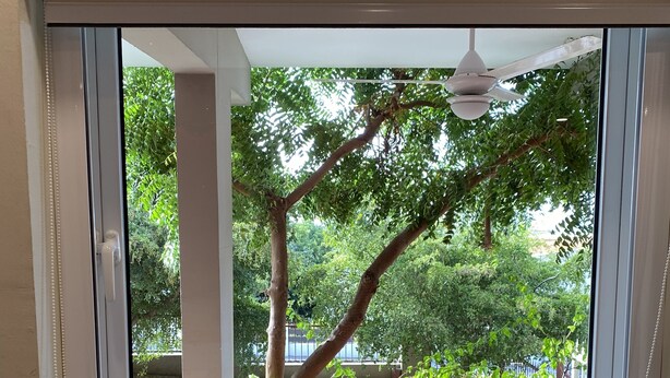 A kitchen with two stainless steel sinks, a window overlooking a deck with a chair, and a ceiling fan. - O Casarao Guesthouse (Willemstad)