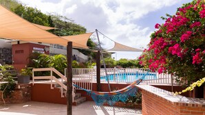 A hammock hanging between two wooden posts, a brick wall, a pool, and a white fence. - O Casarao Guesthouse (Willemstad)