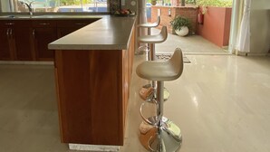 A kitchen with a wooden island, bar stools, a surfboard decoration, and a view of the outdoors. - O Casarao Guesthouse (Willemstad)